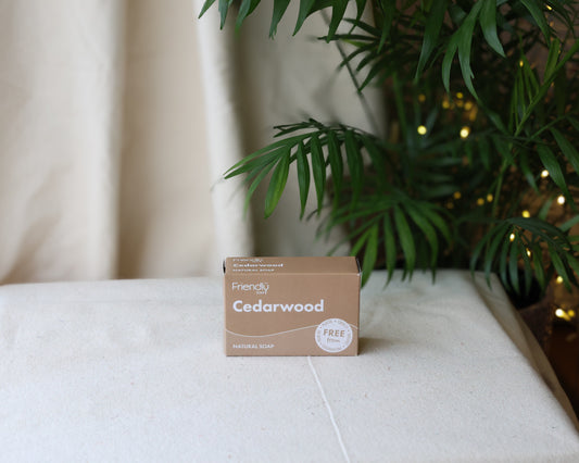 A Cedarwood Soap Bar packaged in a brown box with 'Cedarwood' and 'vegan' printed on the front, placed on a white surface with a plant in the background.
