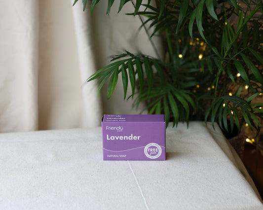 A purple Lavender soap bar with the label 'Lavender' placed on a white surface, with green foliage and a string of lights in the background.