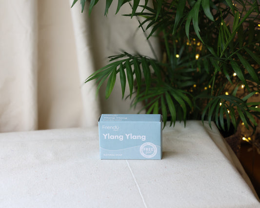A packaged bar of Ylang Ylang soap displayed on a white surface with a plant andIndonesian flagin the background, indicating the tropical origin of the fragrance.