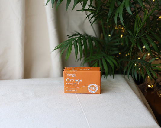 A bar of Orange & Grapefruit Soap placed on a white surface with a plant and some Christmas lights in the background.
