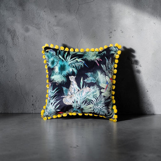 Deepest Jungle velvet cushion with acid yellow pompoms, front view against a deep grey concrete wall