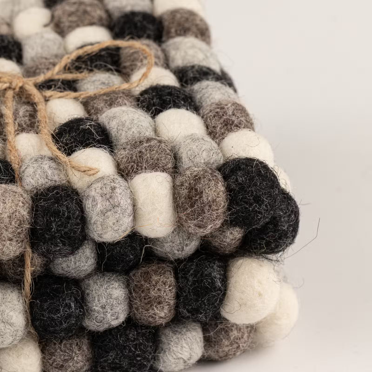 Close-up of stacked grey felt ball coasters tied with jute twine, showing charcoal, grey, taupe and cream wool balls