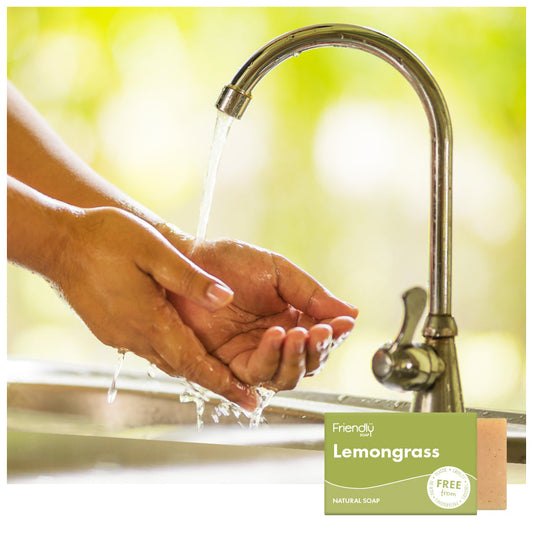 Hand washing with running water from a faucet, next to a bar of Friendly Soap labeled 'Lemongrass'.