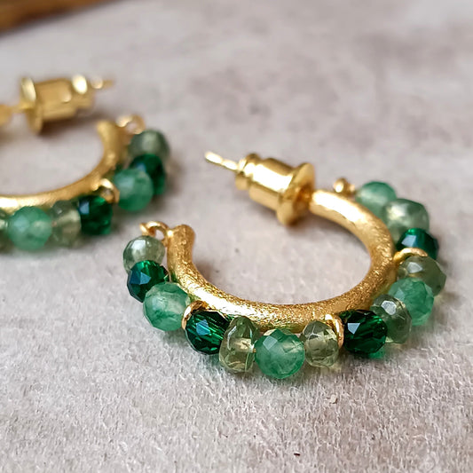 Gold hoop earrings with green gemstones on a light gray surface