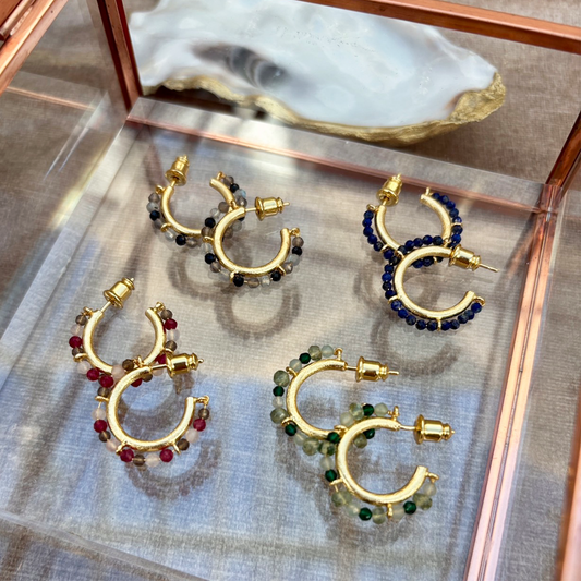 Gold hoop earrings with colorful beads on a reflective surface