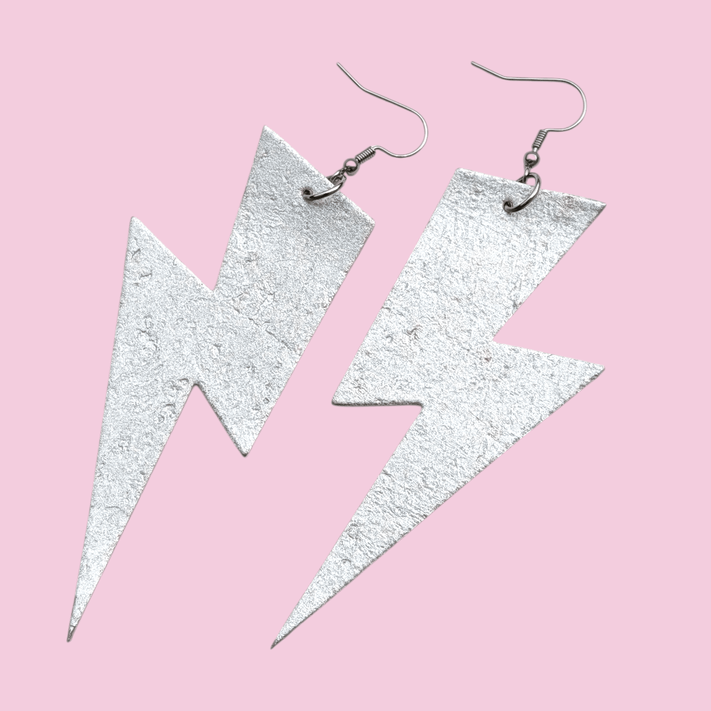 Silver lightning bolt earrings on a pink background