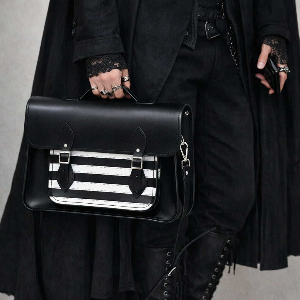 Person holding a black satchel with a striped pattern, wearing a dark coat and boots.