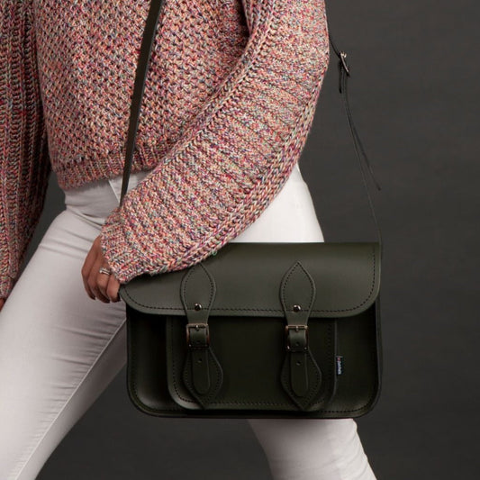 Person holding a black leather satchel bag against a dark background