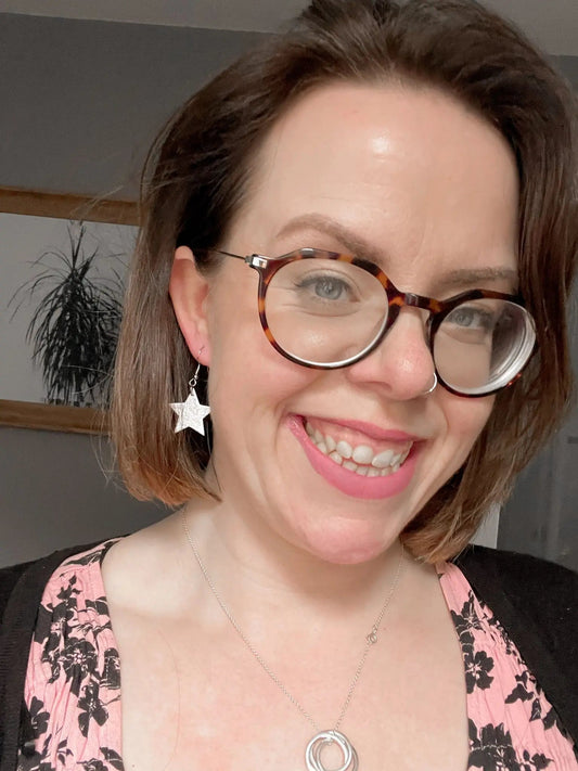 Woman wearing glasses with a star-shaped earring and pink lipstick indoors.