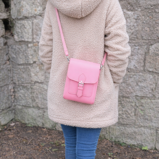 Person wearing a beige coat with a pink crossbody bag against a stone wall.