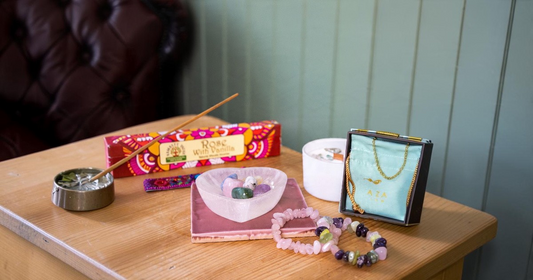 Mindful Christmas gift ideas on a wooden table: Rose & Vanilla incense, a heart-shaped bowl of polished crystals, a candle and crystal chip bracelets