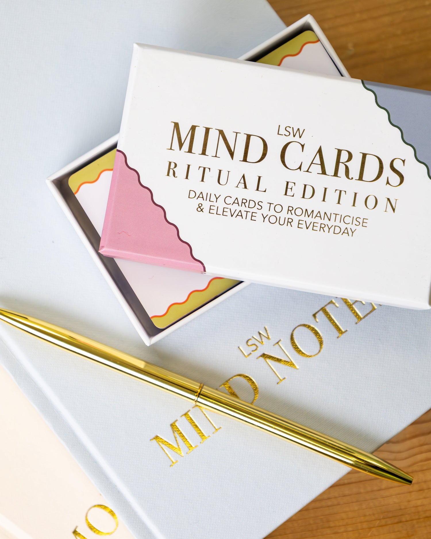 LSW Mind Cards Ritual Edition box open to reveal colourful daily affirmation cards, styled with an LSW Mind Notes journal and gold pen on a wooden surface