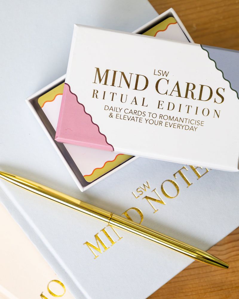 LSW Mind Cards Ritual Edition box open to reveal colourful daily affirmation cards, styled with an LSW Mind Notes journal and gold pen on a wooden surface