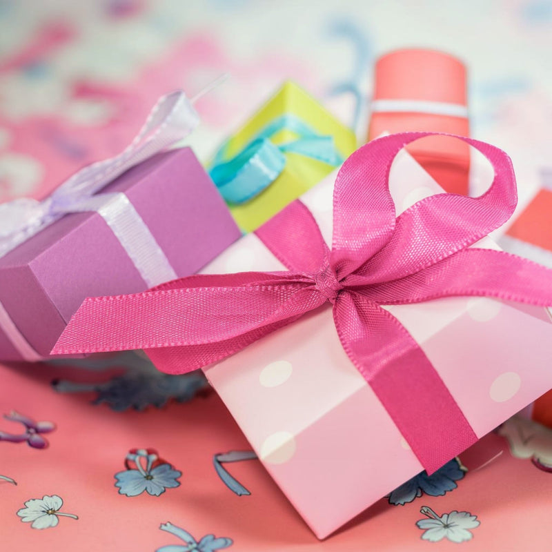 Pastel mini gift boxes wrapped in pink, purple and green ribbons on a floral background — Apricot Moon Gifts Under £10.