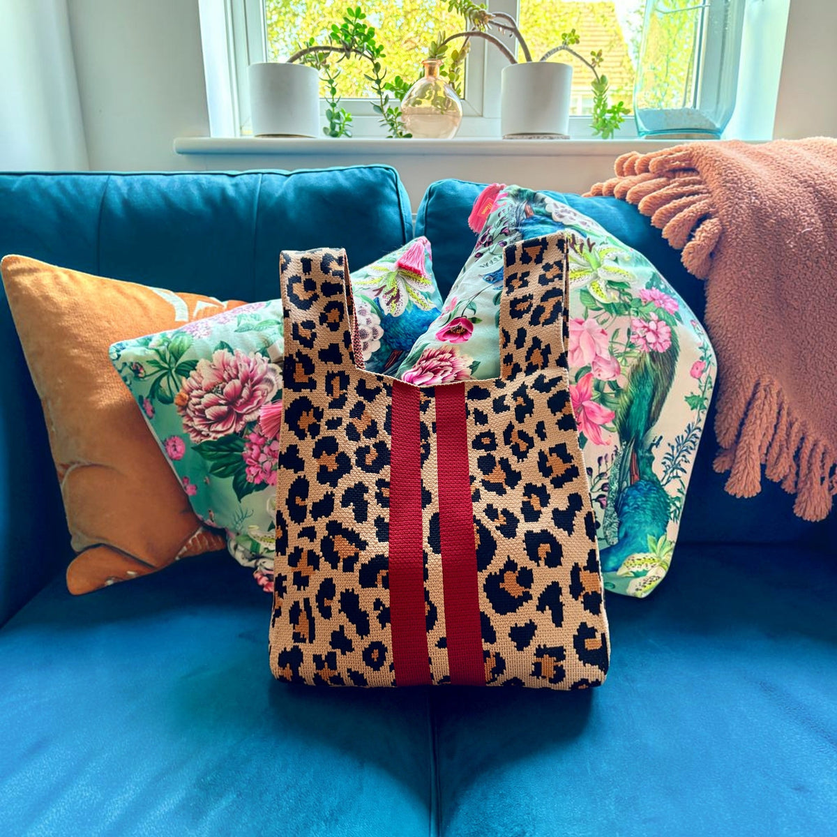 Leopard print knitted tote bag with red stripes on a teal sofa with floral cushions