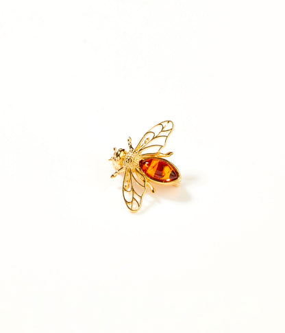 Gold bee-shaped brooch with amber-colored body on a white background