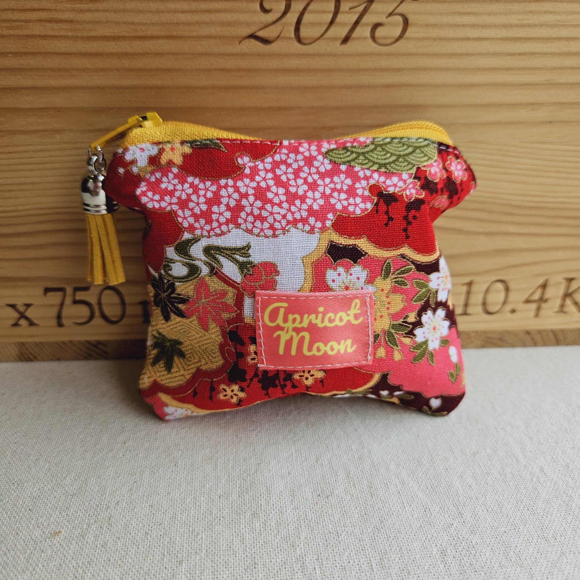 Small fabric pouch with floral design and 'Apricot Moon' label on a textured surface.