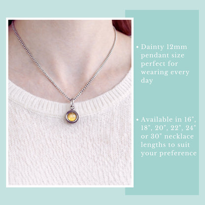 Necklace with a pendant on a person wearing a white sweater, against a light blue background.