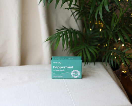 A bar of Peppermint & Poppyseed Soap placed on a white surface with a plant in the background.