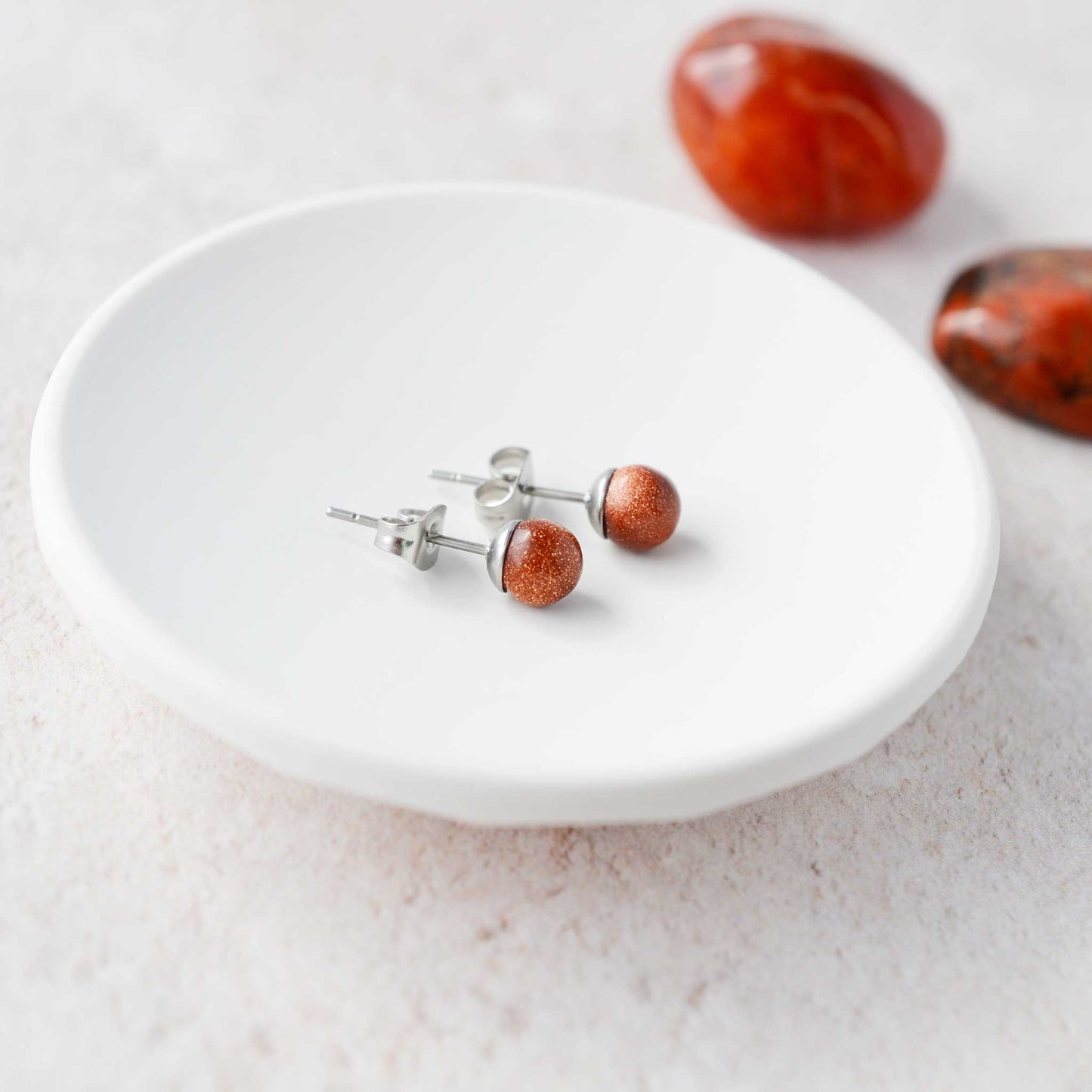 Pair of red stone stud earrings on a white plate with stones in the background