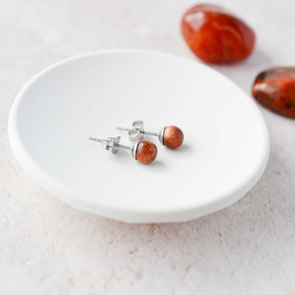 Pair of red stone stud earrings on a white plate with stones in the background