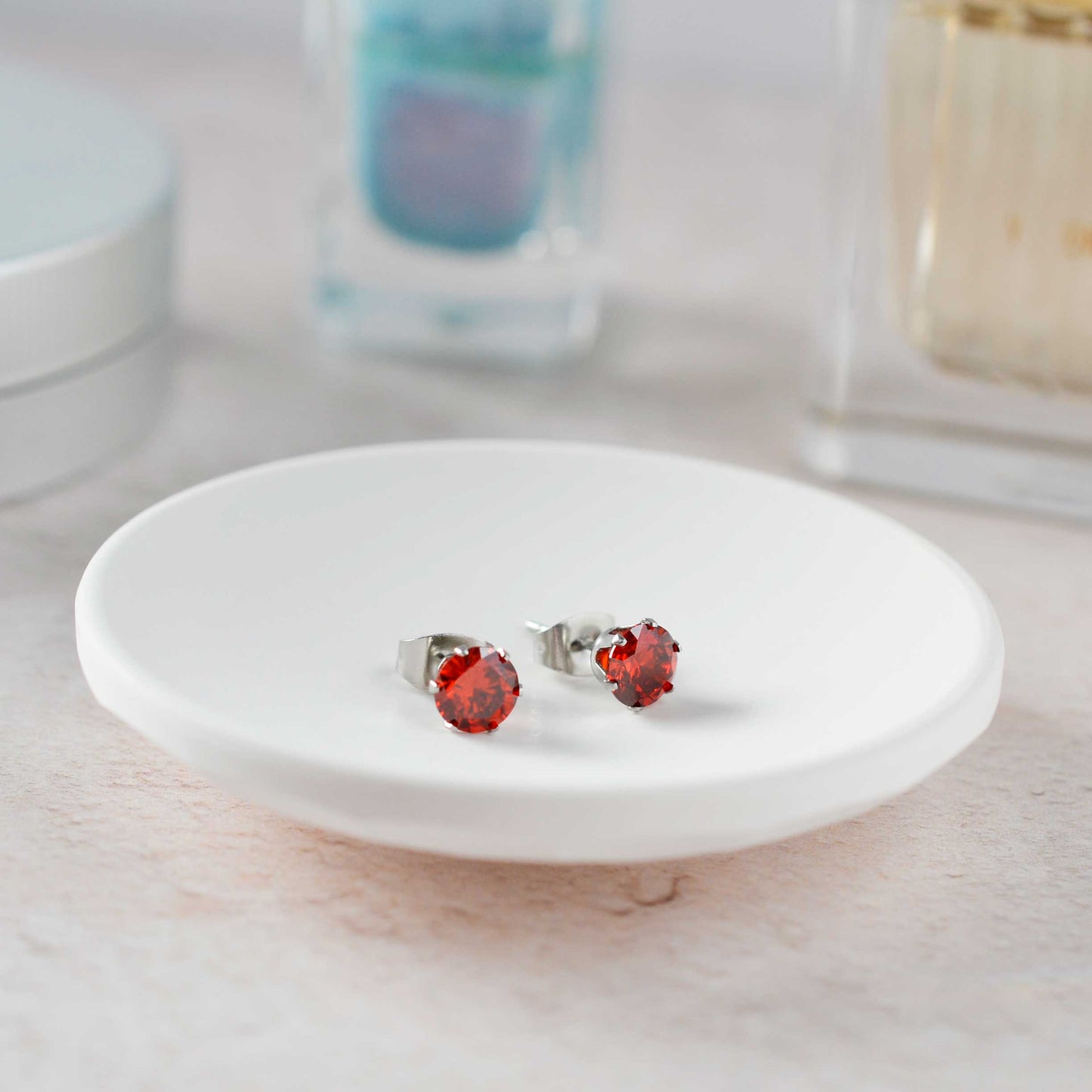 Red gemstone stud earrings on a white dish with a blurred background
