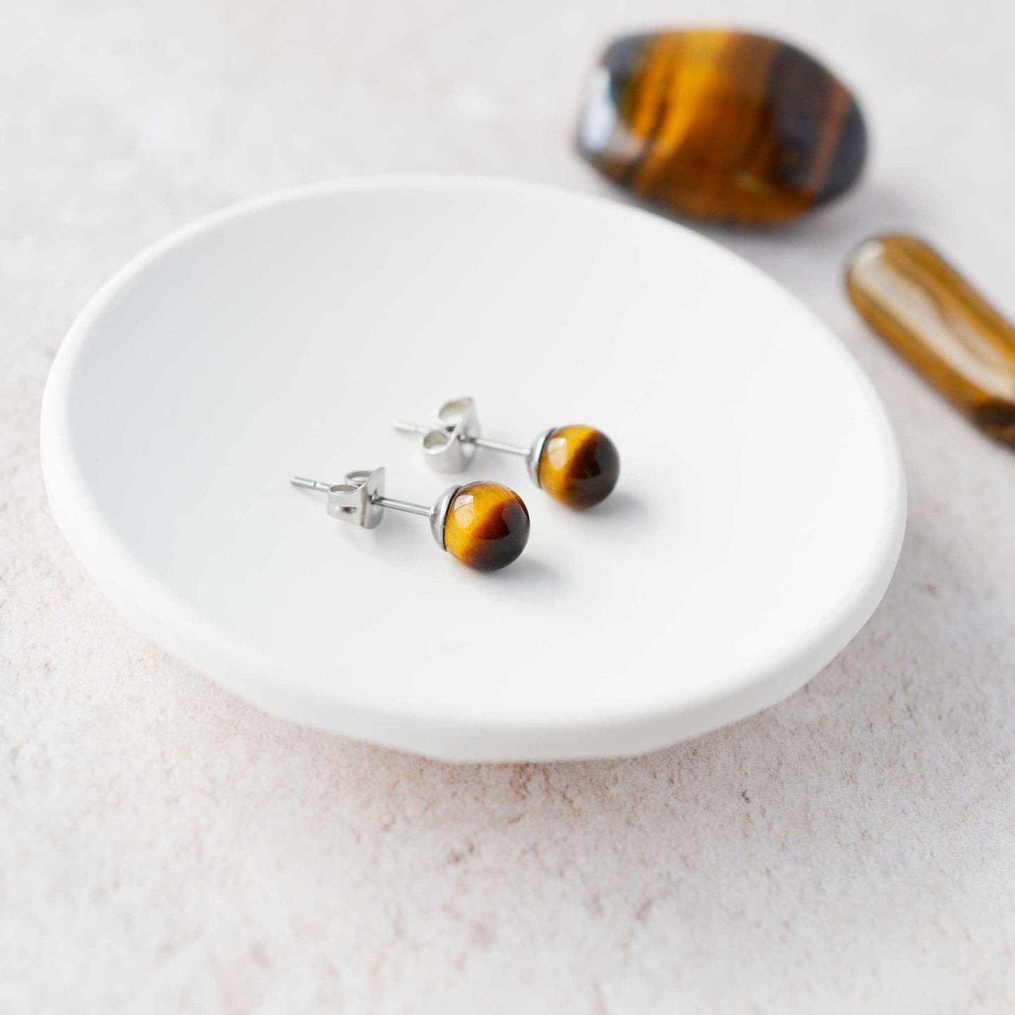 Tiger eye stud earrings on a white dish with tigers eye stones in the background