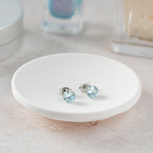 Pair of silver earrings with blue gemstones on a white ceramic dish.