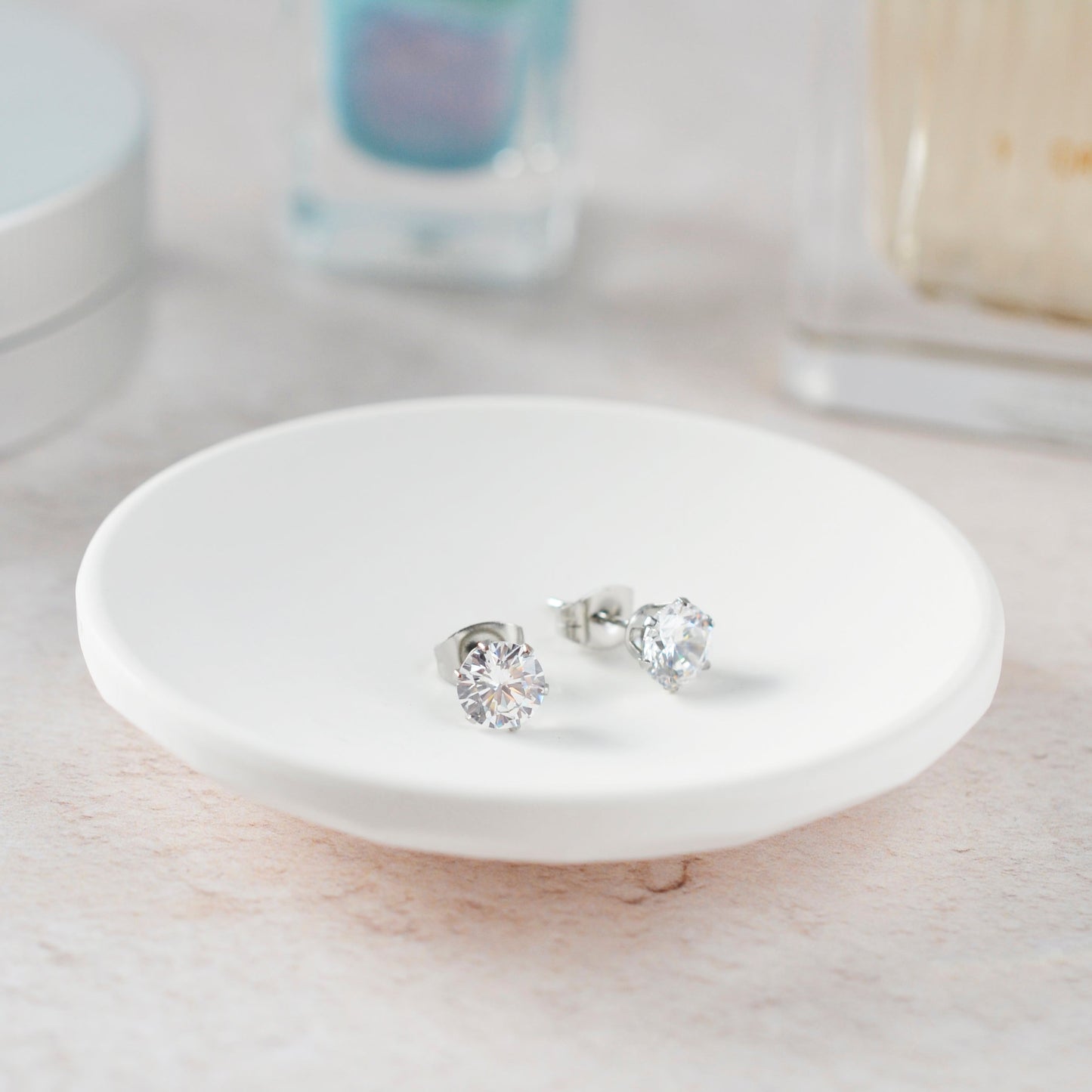 Silver earrings on a white ceramic dish with a blurred background