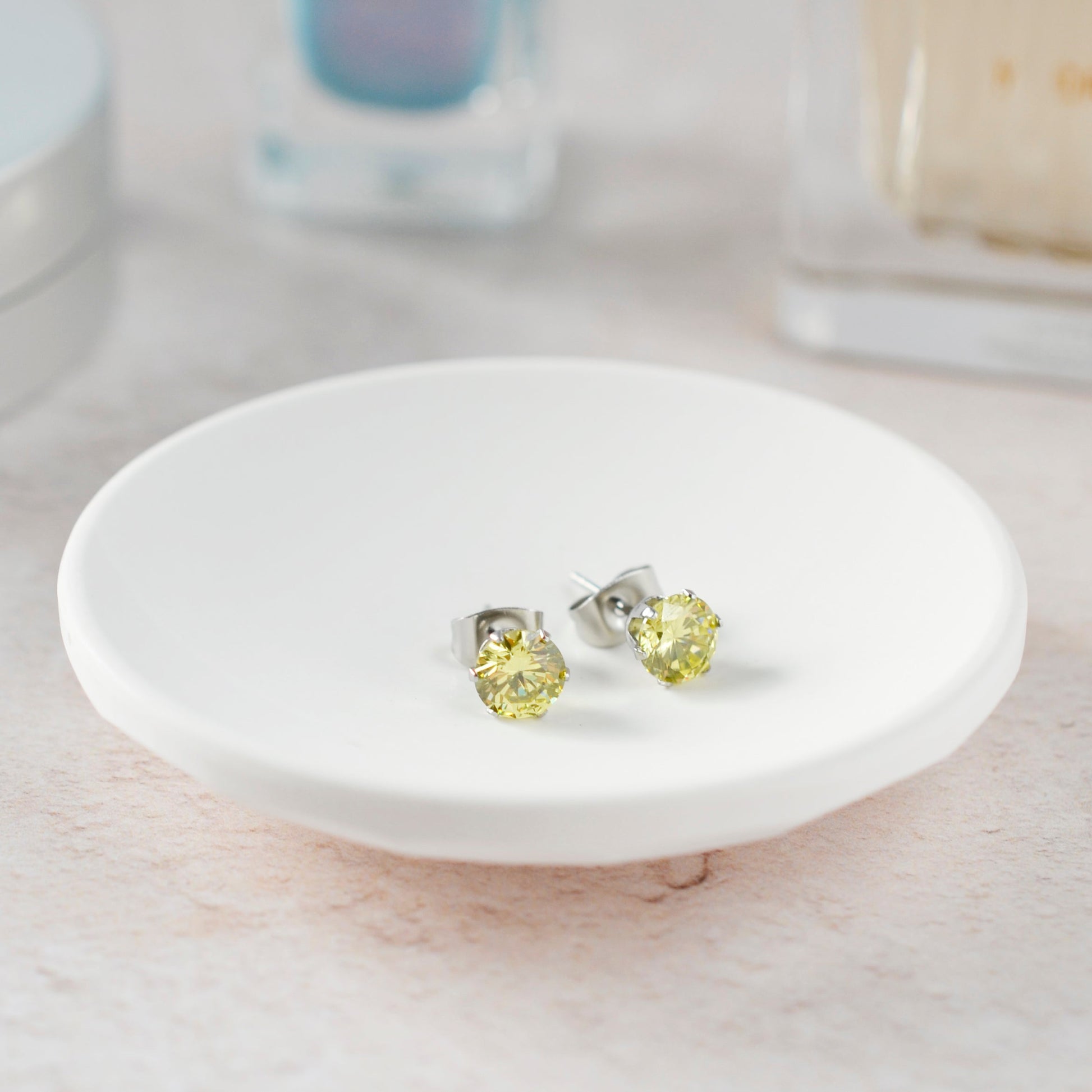 Yellow gemstone stud earrings on a white dish with a blurred background