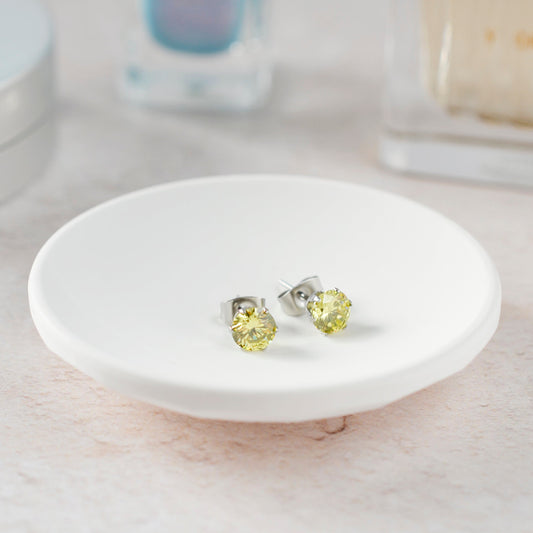 Yellow gemstone stud earrings on a white dish with a blurred background