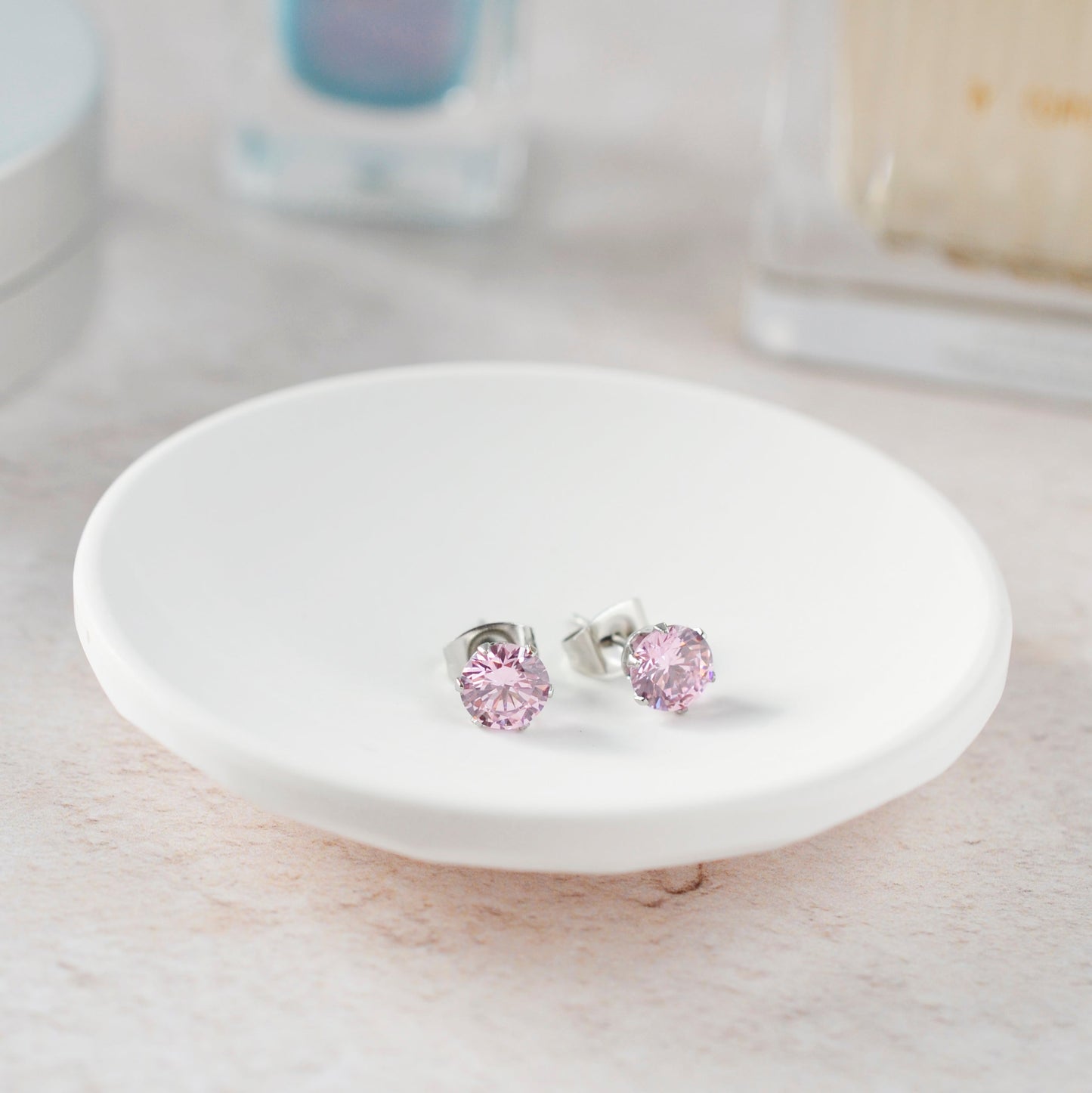 Pink stud earrings on a white ceramic stand with a blurred background