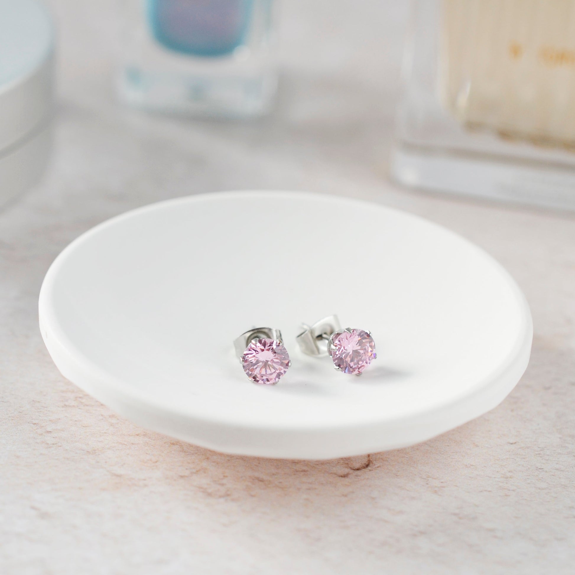 Pink stud earrings on a white ceramic stand with a blurred background