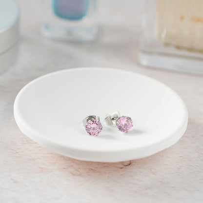 Pink stud earrings on a white ceramic stand with a blurred background