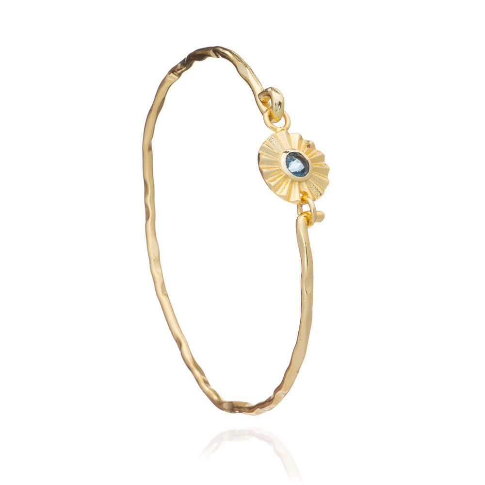 Gold bracelet with a sunflower design and blue gemstone on a white background