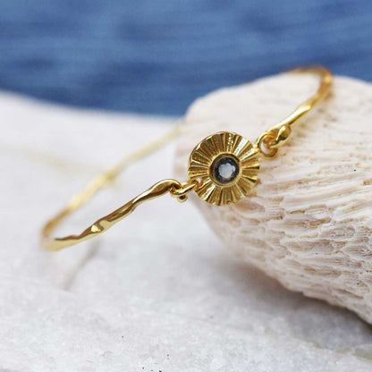 Gold bracelet with a central gemstone on a shell against a blue background