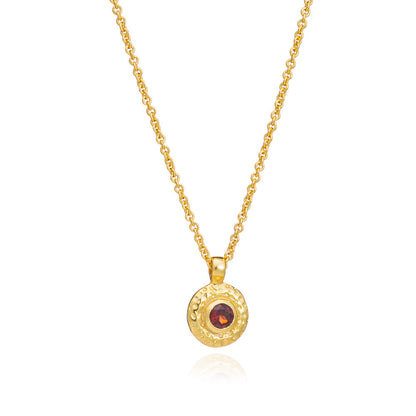 Gold necklace with a round pendant featuring a red gemstone on a white background