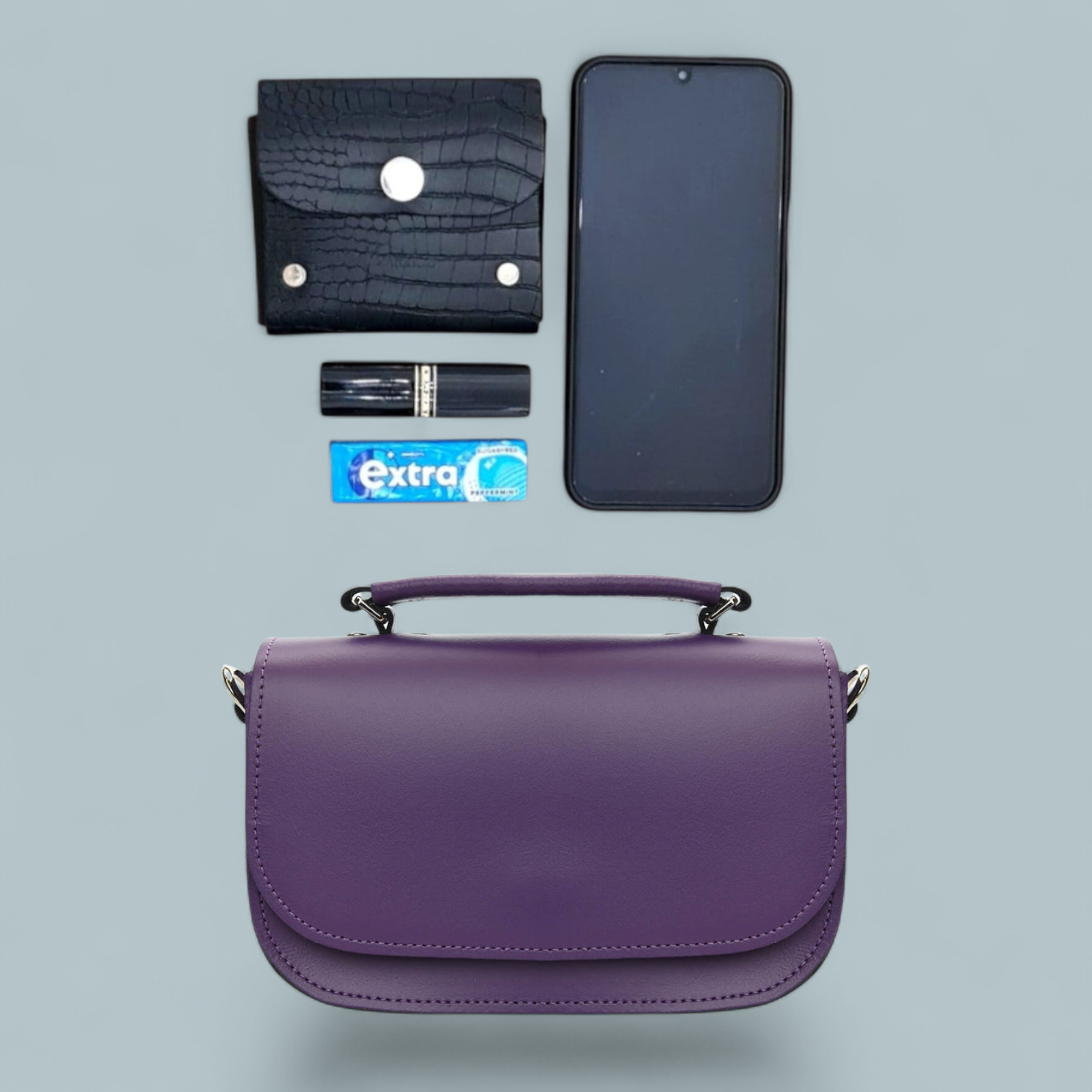 Purple handbag with phone, wallet, lipstick, and gum on a light gray background