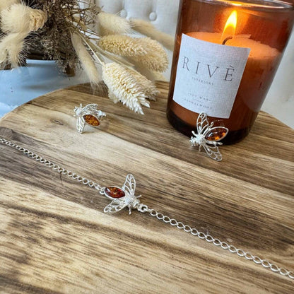 Silver jewelry with amber stones on a wooden surface next to a lit candle labeled 'RIVE'.