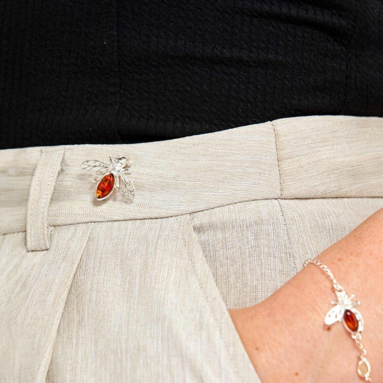 Close-up of a person wearing a silver brooch with a red gemstone on a light-colored outfit.