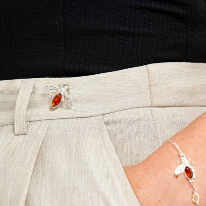 Close-up of a person wearing a silver brooch with a red gemstone on a light-colored outfit.
