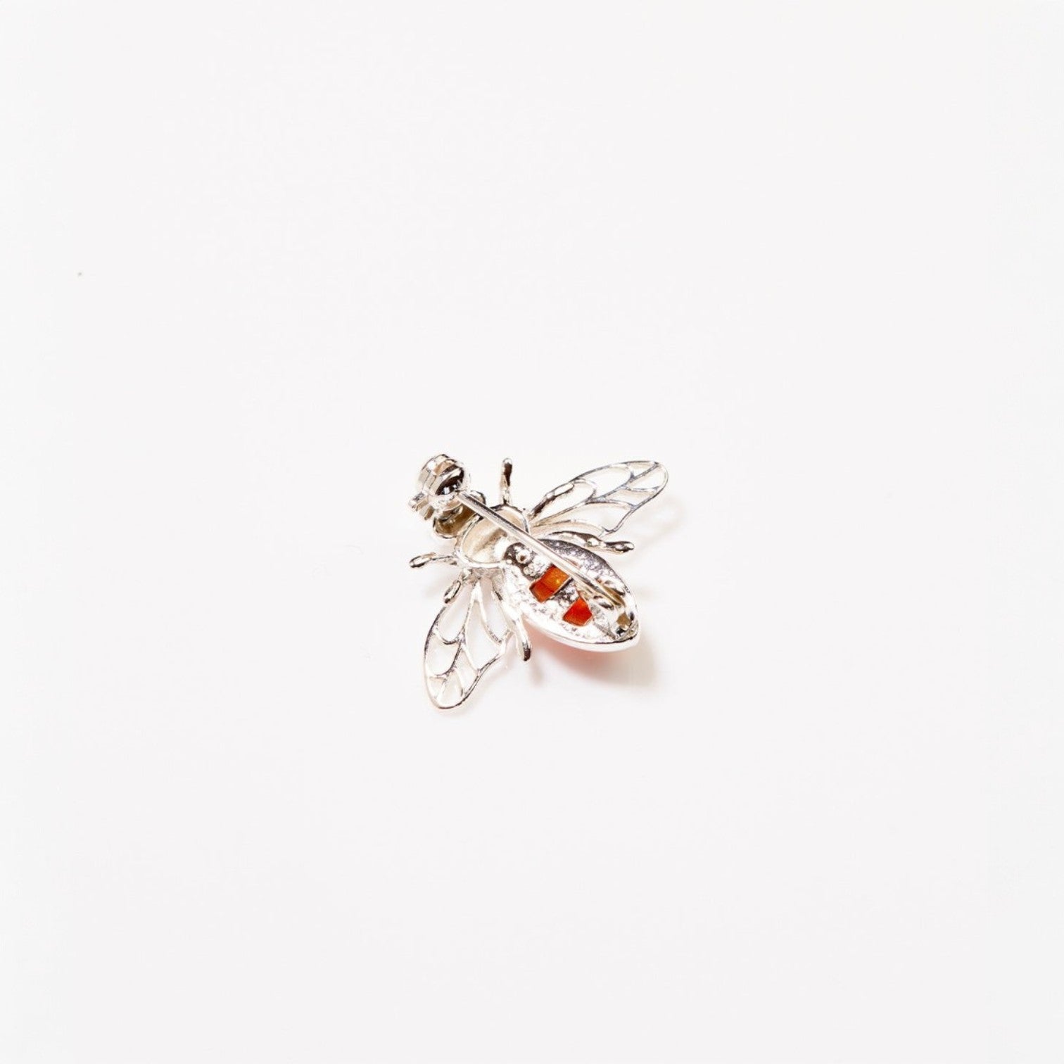 Silver bee-shaped brooch with red gemstones on a white background