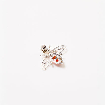 Silver bee-shaped brooch with red gemstones on a white background