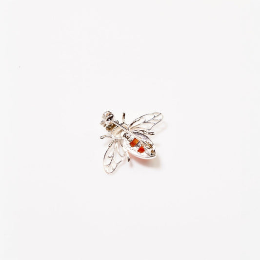 Silver bee-shaped brooch with red gemstones on a white background