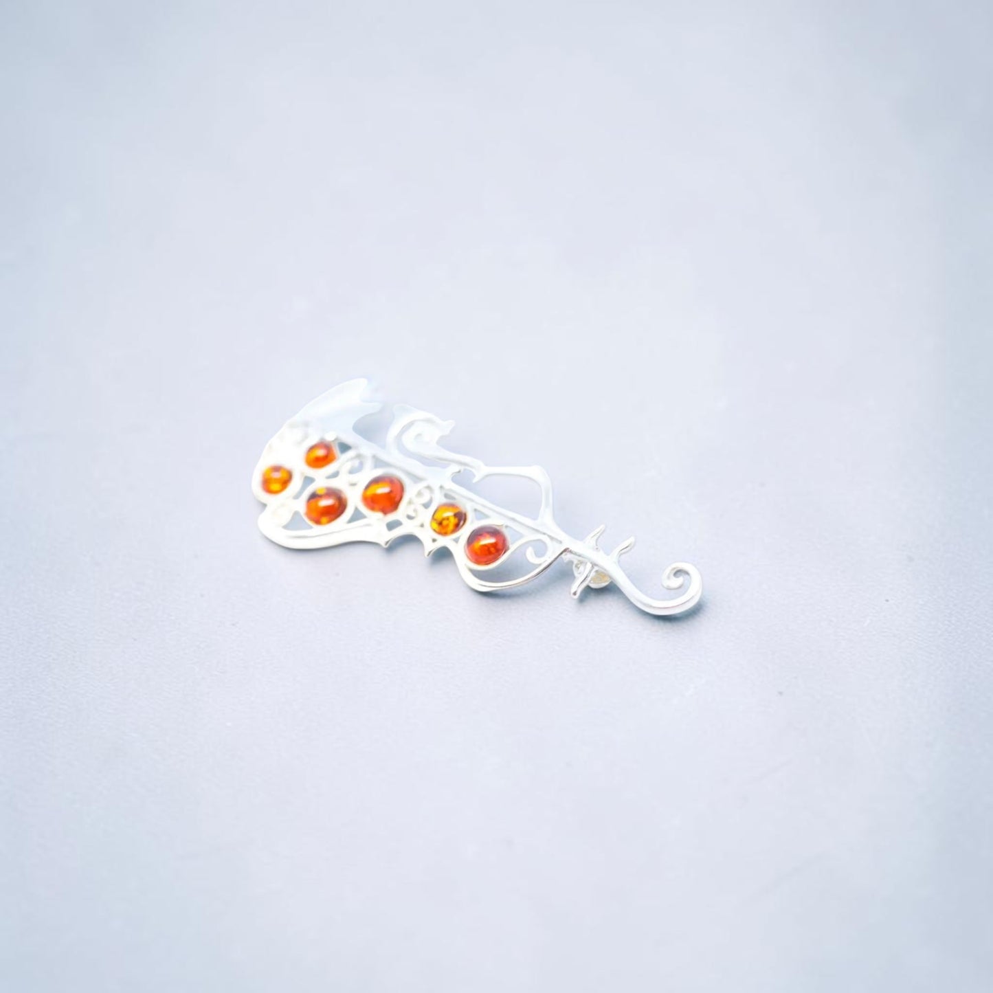 A silver filigree hair claw clip with five small orange and red cabochon gemstones, shown on a light gray background.