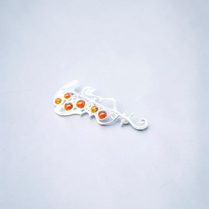 A silver filigree hair claw clip with five small orange and red cabochon gemstones, shown on a light gray background.