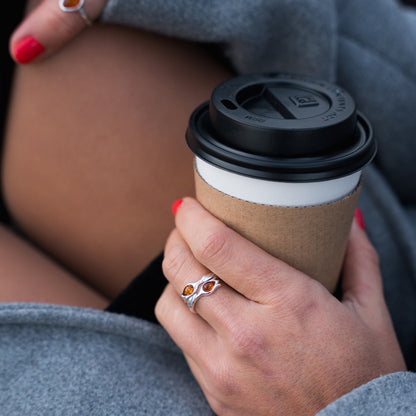 Person holding a paper coffee cup with a black lid, wearing a ring with a red stone.