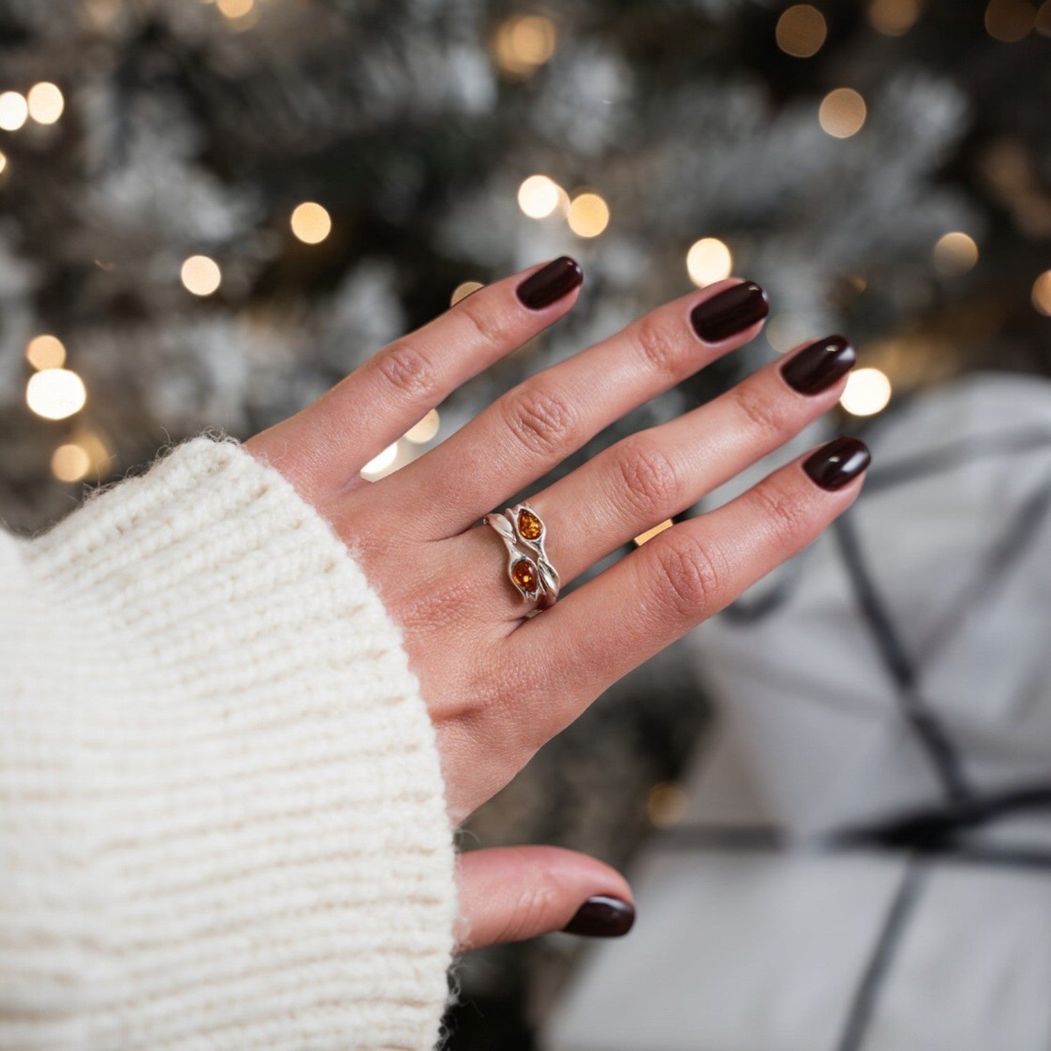 Hand with dark nail polish wearing a silver ring against a blurred festive background
