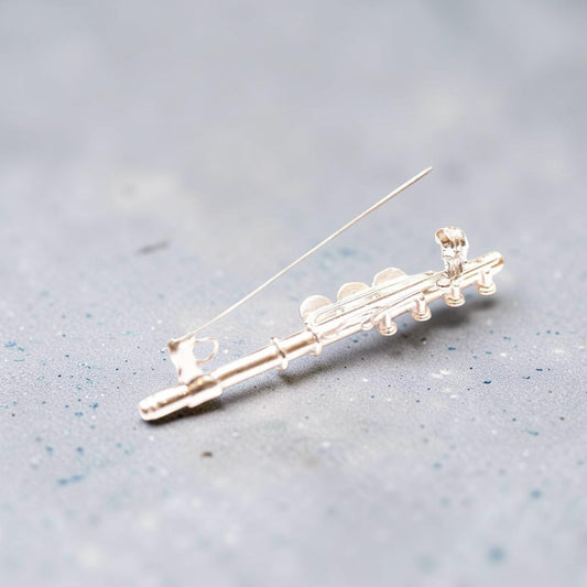 A silver flute-shaped brooch with a thin pin back, displayed on a textured gray surface.