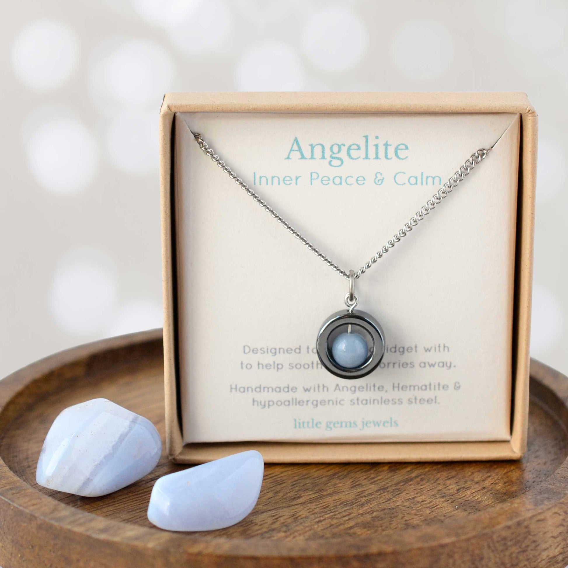 Necklace with pendant and stones in a box labeled 'Angelite' on a wooden surface.